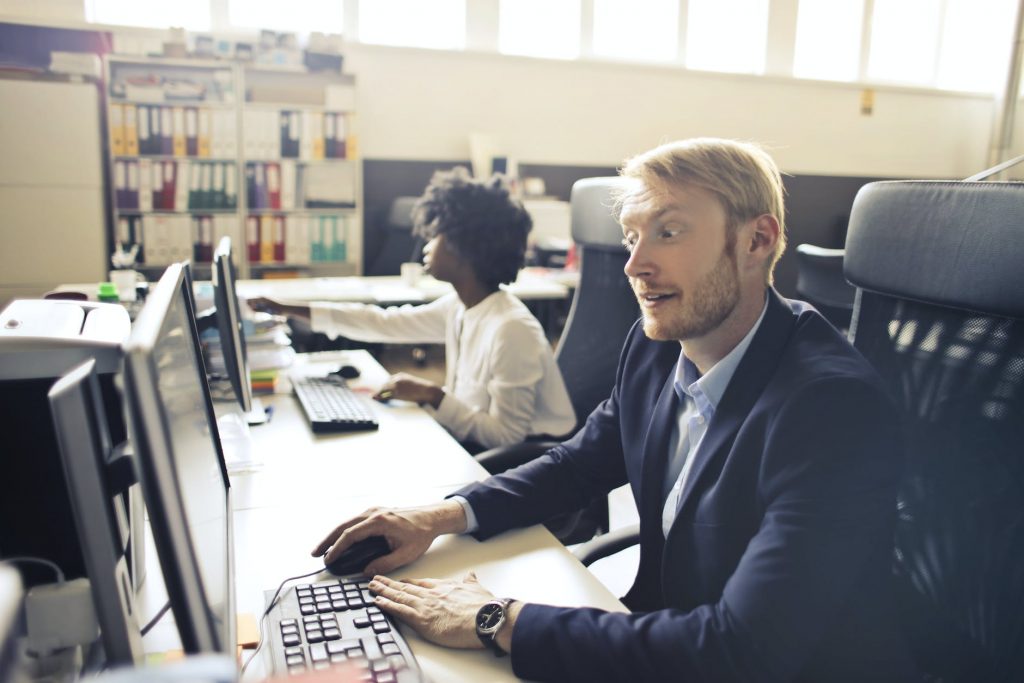 adult surprised executive man using computer beside ethnic colleague in open space office